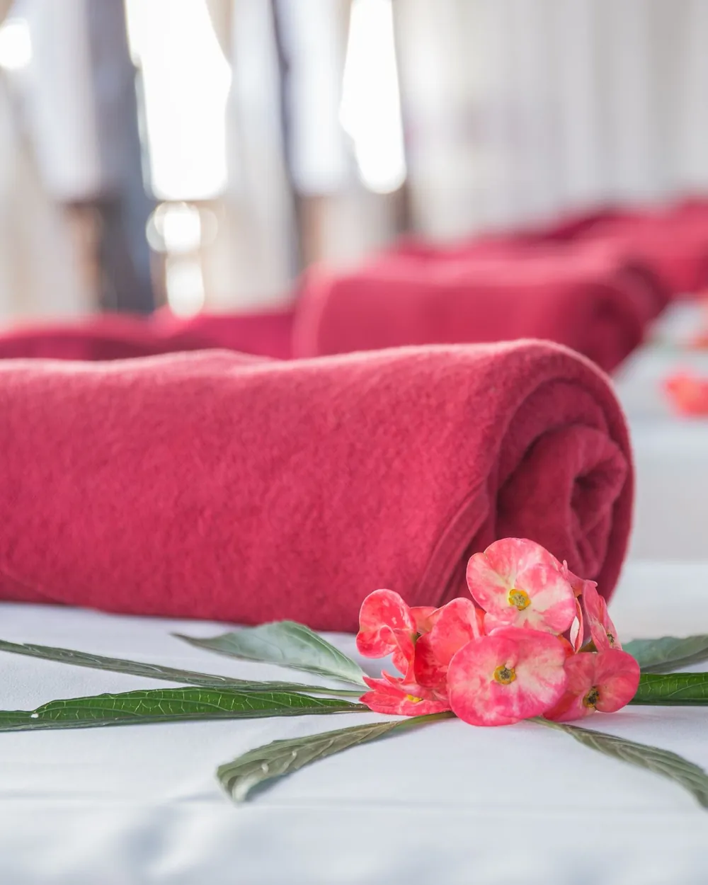 Serviette roulée et fleurs roses posées sur une table de soin